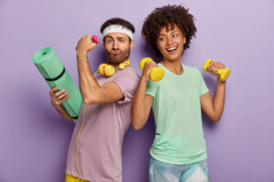 glad-multi-ethnic-fitness-husband-wife-attend-sport-center-exercise-with-dumbbells-hold-fitness-mat-stand-back-each-other-have-funny-happy-looks-fitness-