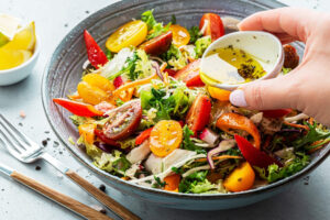 A vibrant vegetable bowl with a hand pouring Figro olive oil.